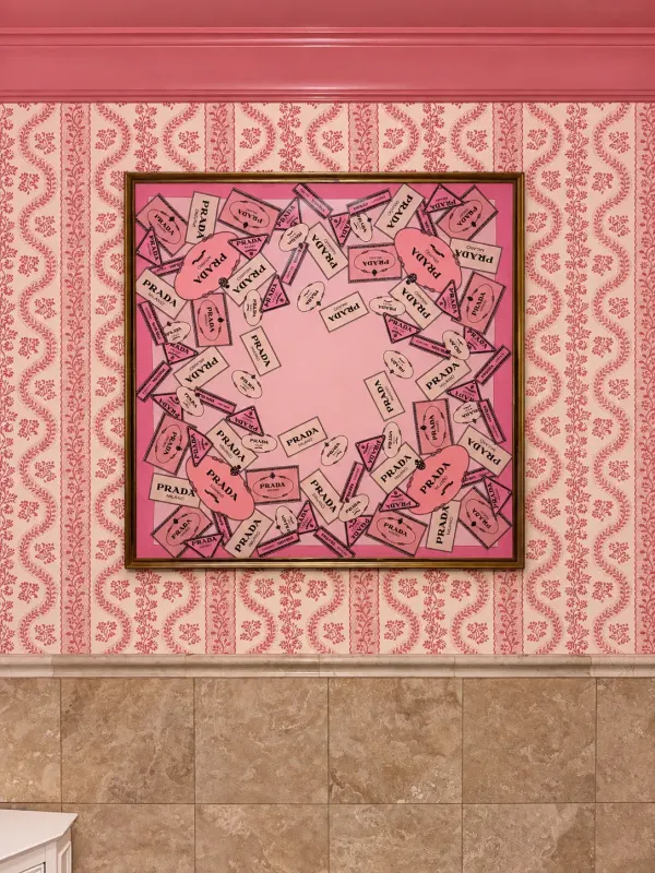 Close detail of framed fashion-label artwork against pink patterned wallpaper